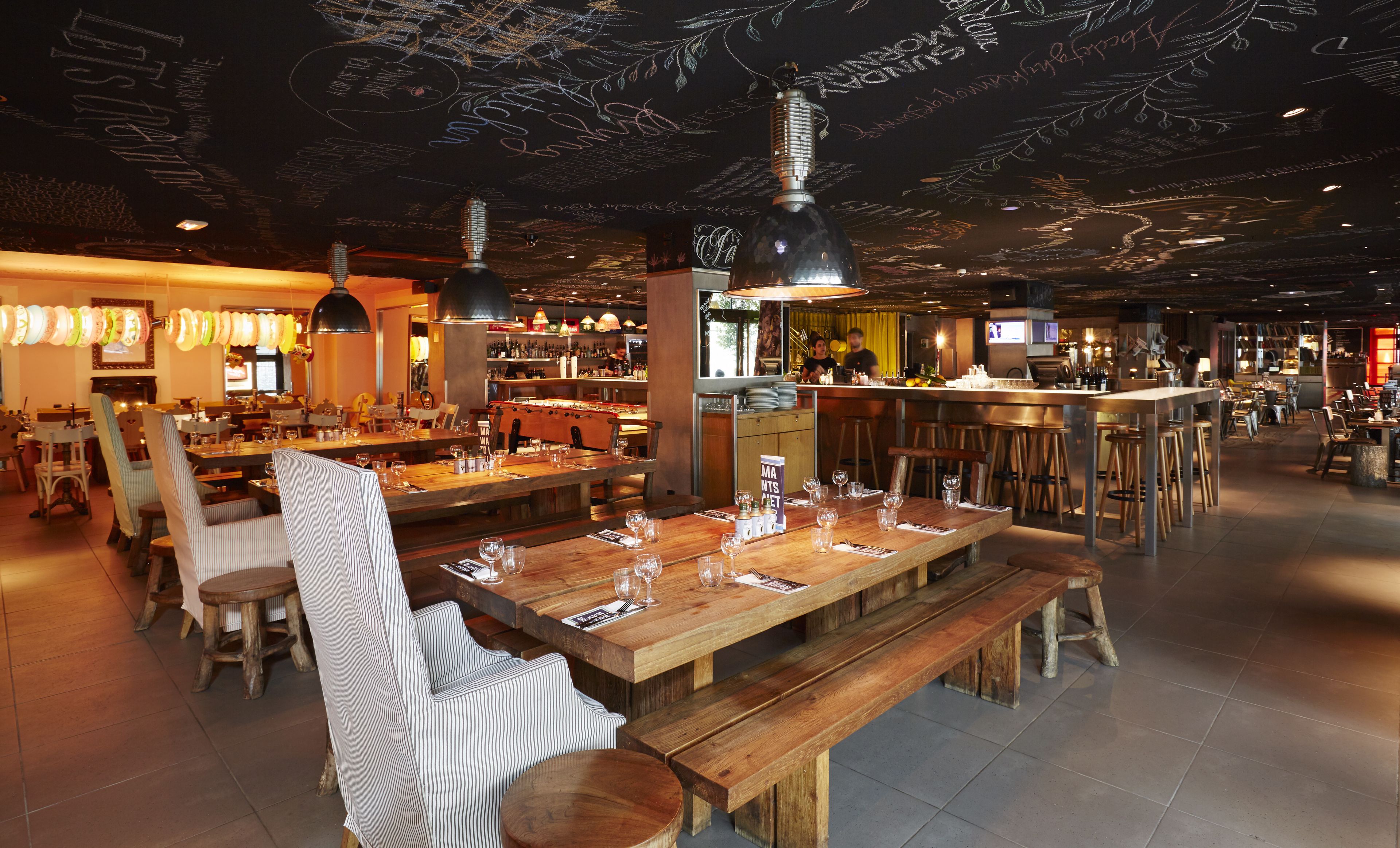 Ein Restaurant mit Holztischen und -stühlen, einer Bar und einer kunstvoll gestalteten Decke.
