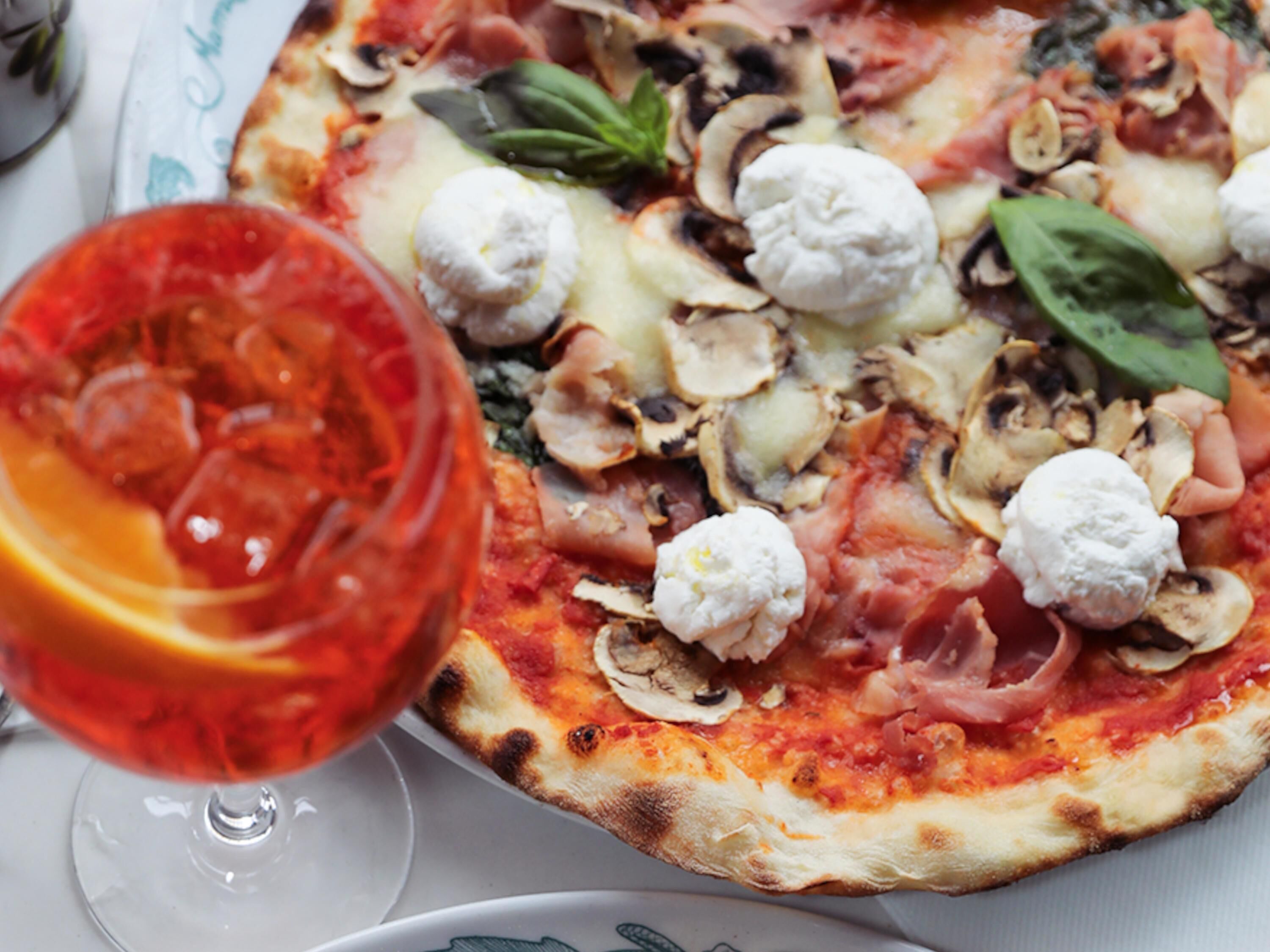 A pizza with toppings and a glass of red drink on a table.