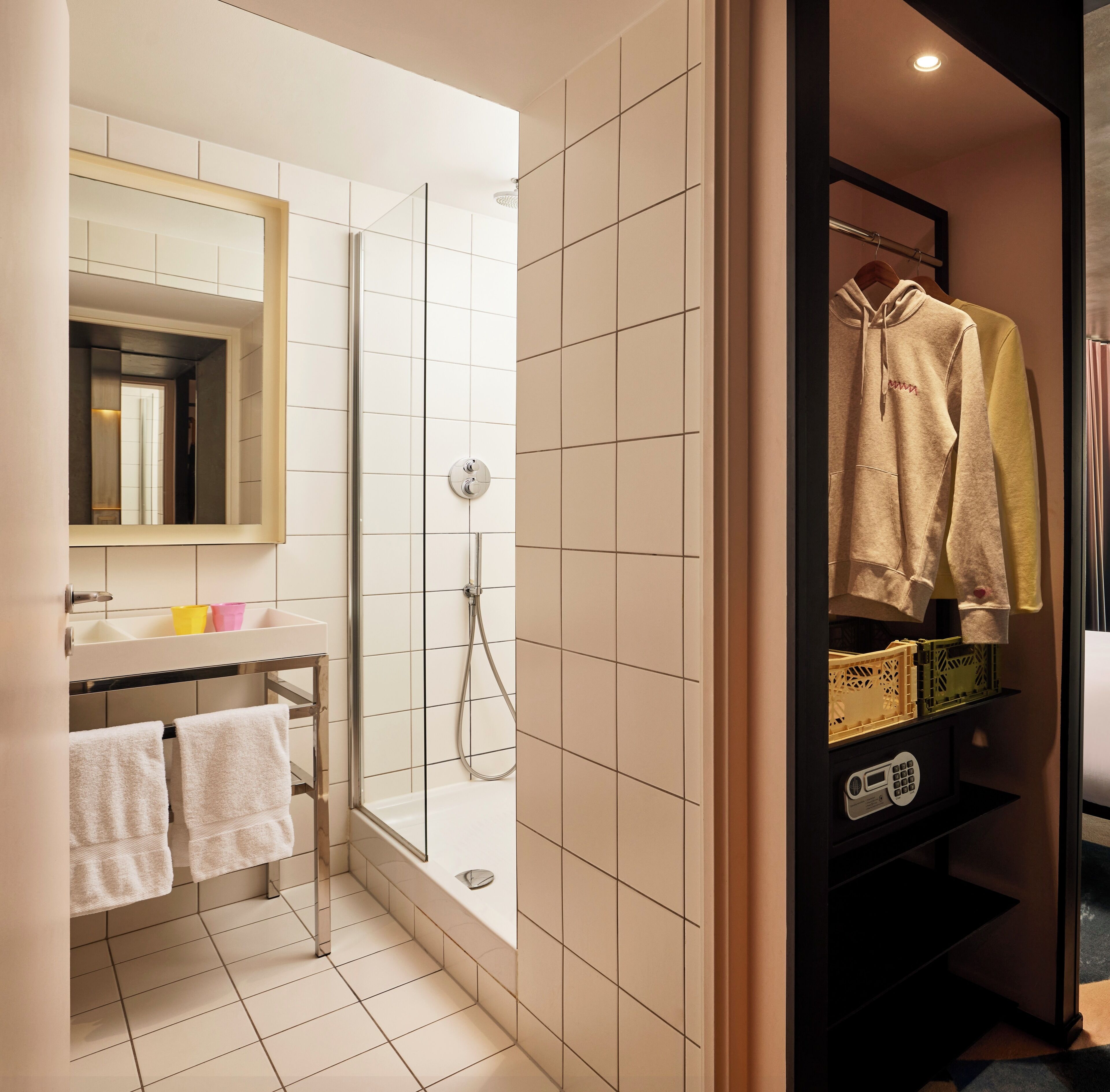 Een moderne badkamer met een douchecabine van glas, een wastafel met spiegel en een kledingrek met casual kleding.