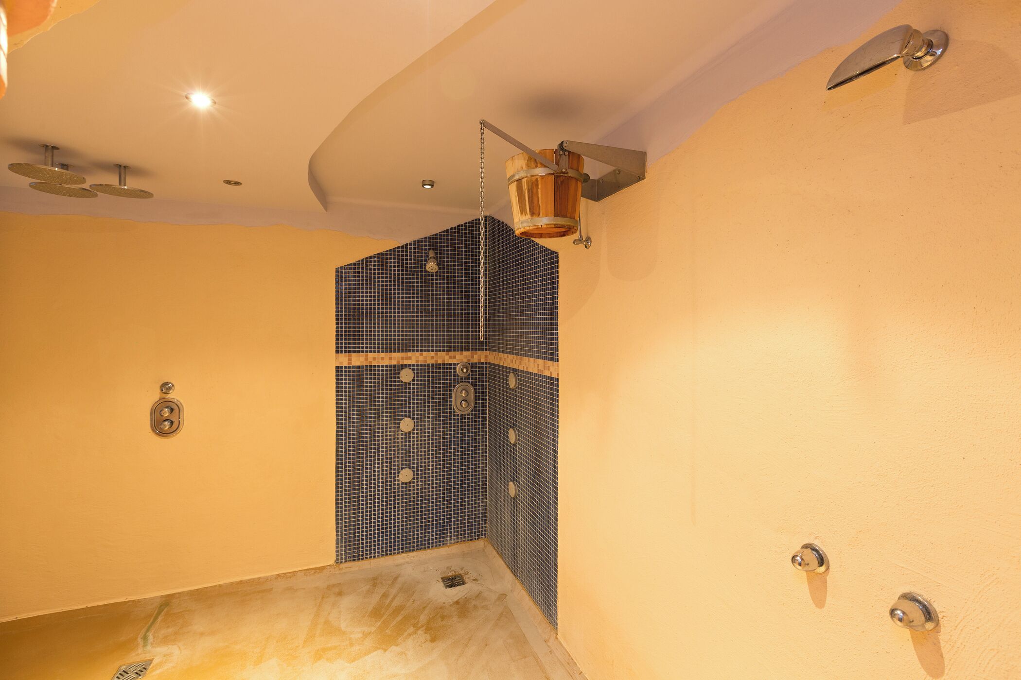 Une salle de bain avec un mur de douche recouvert de carreaux bleus, un seau en bois servant d’élément décoratif et un luminaire au plafond.
