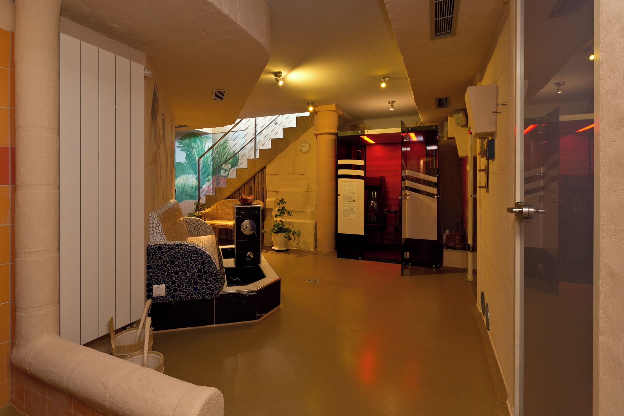 A modern hotel lobby with a staircase, a reception desk, and a seating area with cushions.