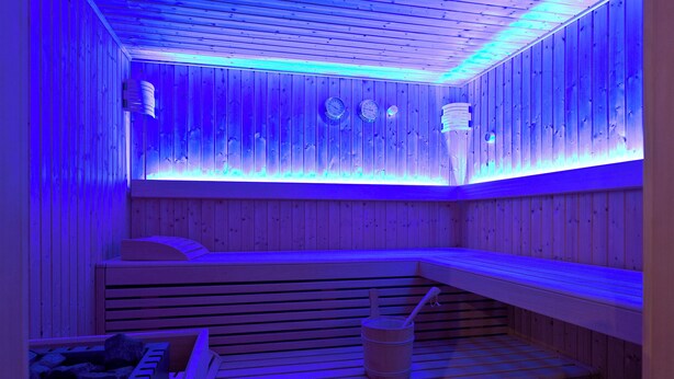 Sauna con bancos de madera y un cubo, iluminada con luces azules.