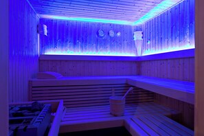 A sauna with wooden benches and a bucket, illuminated by blue lighting.