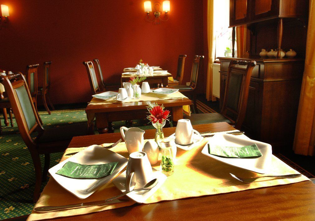 A dining area with tables set for two, each with a white napkin, a glass, and a pitcher. There are chairs around the tables, and a vase with flowers on the table.