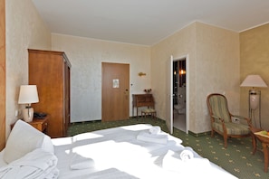 A hotel room with a bed, a wooden wardrobe, a desk with a chair, a lamp, and a bathroom visible through an open door. - Hotel Harmonie (Waren (Müritz))