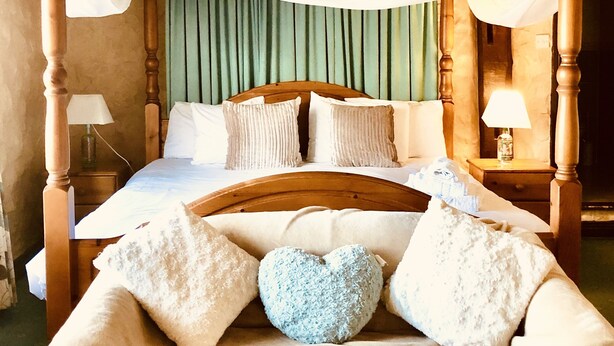 A four-poster bed with a canopy, multiple pillows, a heart-shaped cushion, and bedside lamps. - The Horseshoe Inn (Hailsham)