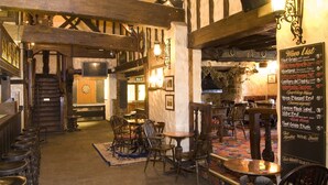 A rustic pub interior with exposed wooden beams, stone flooring, and a traditional pub layout including tables and chairs. - The Horseshoe Inn (Hailsham)