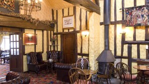 A traditional inn with exposed wooden beams, a patterned carpet, and a large fireplace. - The Horseshoe Inn (Hailsham)