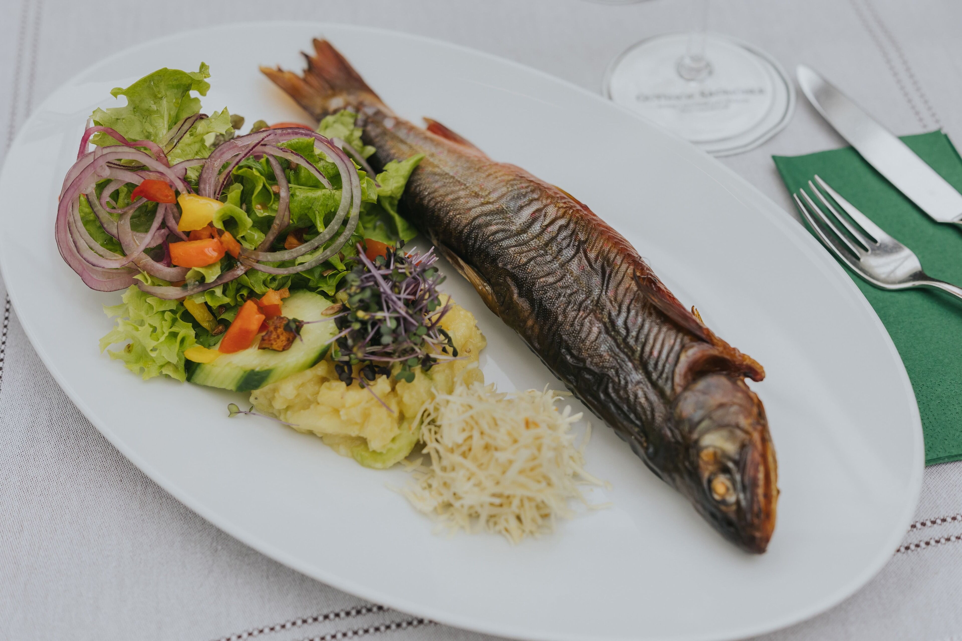 Um prato com um peixe inteiro, salada e purê de batatas.