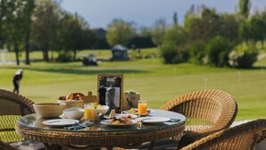 A dining table set with breakfast items, a menu, and a view of a golf course. - Gutshof Sagmuehle (Bad Griesbach im Rottal)
