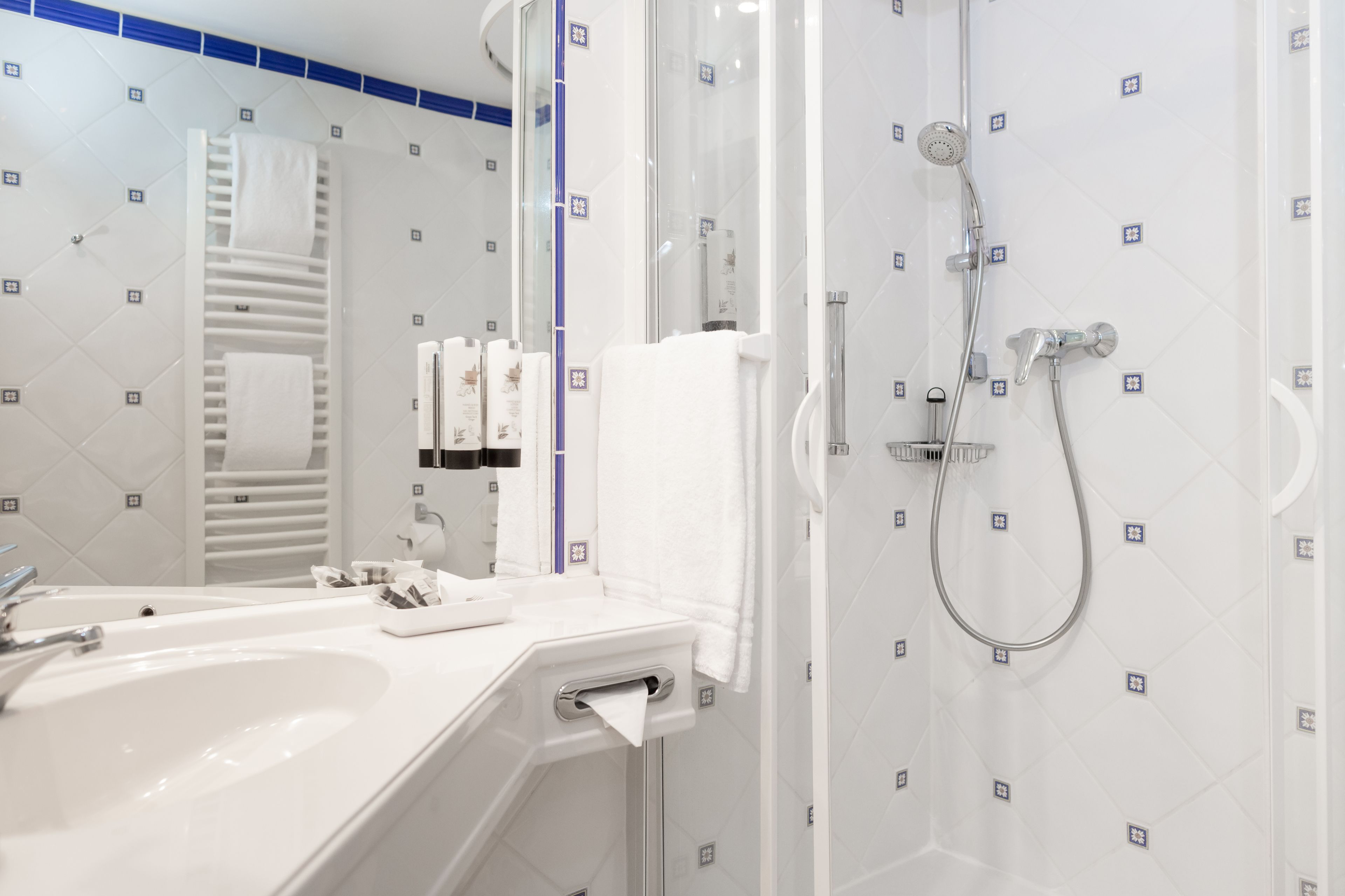 A modern bathroom with a white sink, a mirror, a towel rack, and a shower area.