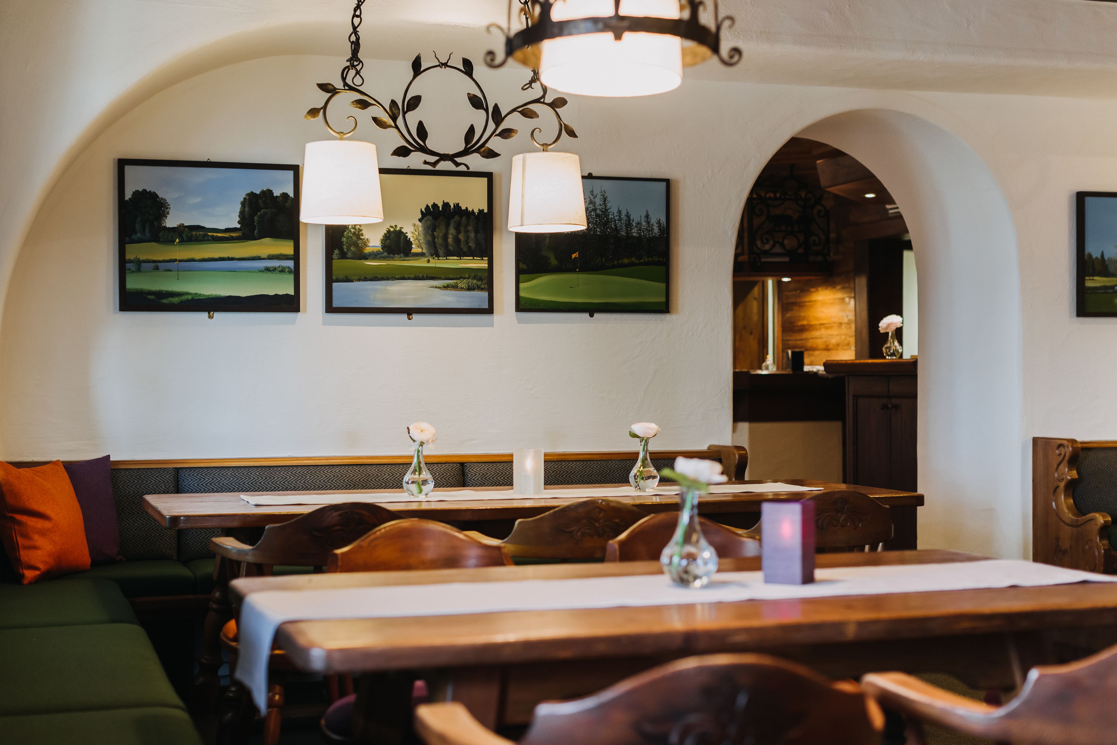Een restaurantinterieur met houten tafels, comfortabele zitplaatsen en golfbaanfoto's in lijsten aan de muur.