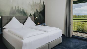 Una habitación de hotel con cama, mesita de noche, ventana con vistas a un parque y un cuadro en la pared.