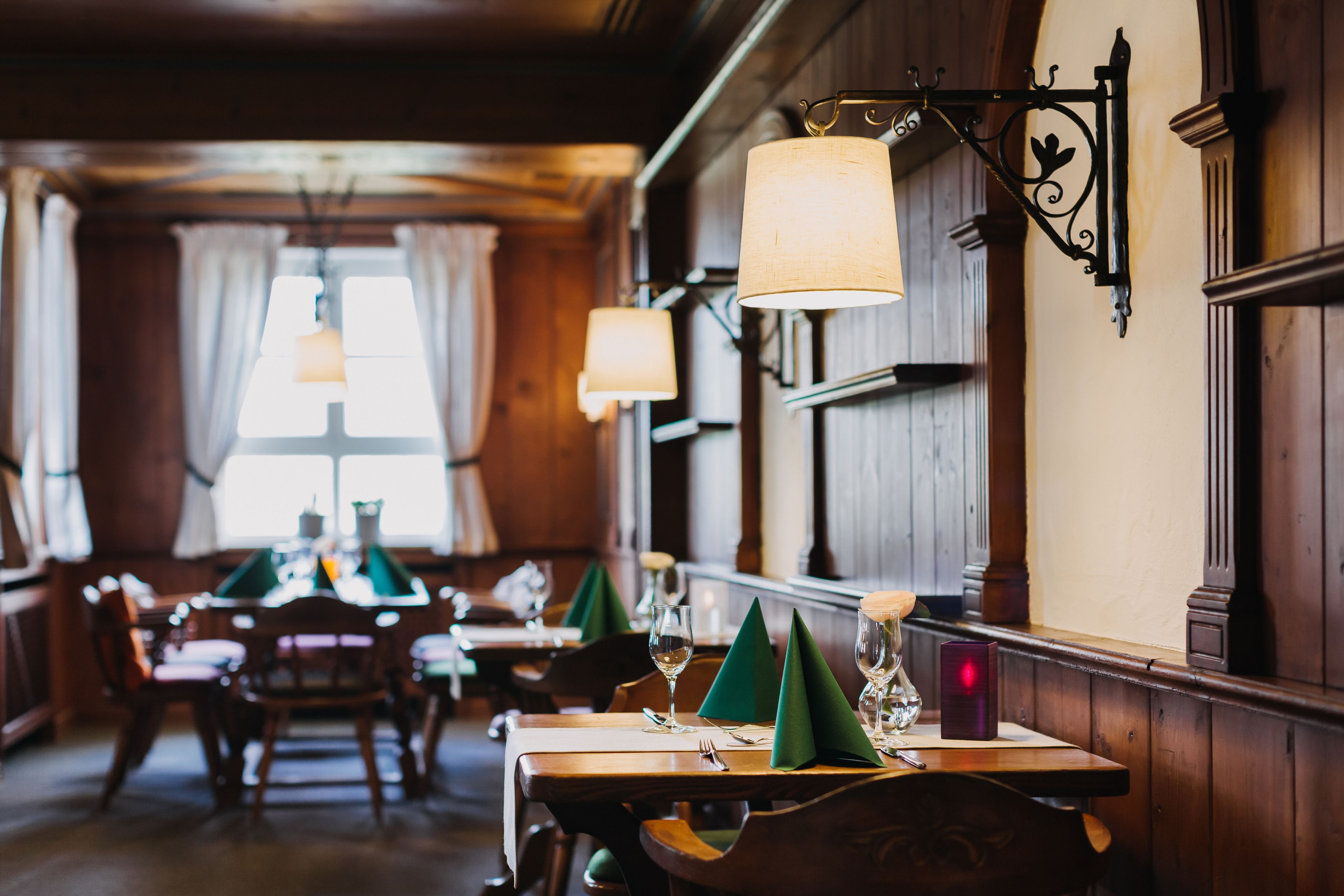 Ein Restaurantinnenraum mit Holzwandverkleidung, grünen Tischdecken und tischlichter Kerzen.