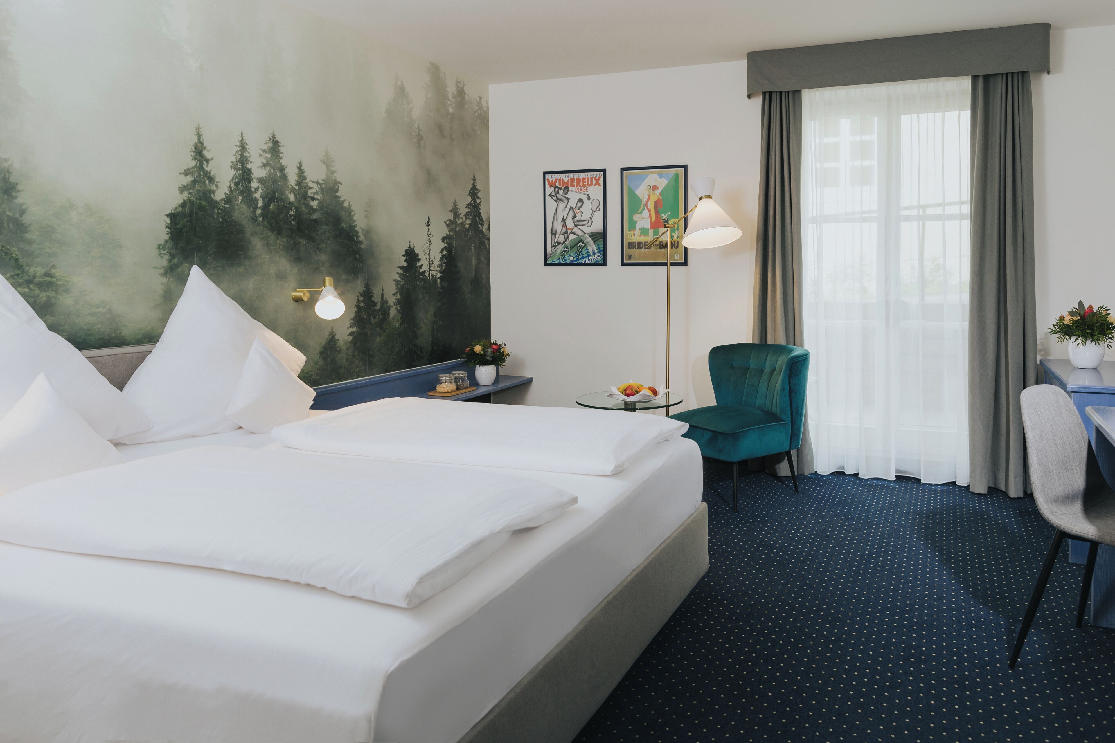 A hotel room with a bed, a desk, a chair, a lamp, and a painting on the wall.