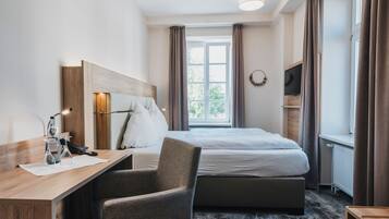 Une chambre d’hôtel équipée d’un lit, d’un bureau, d’une chaise, d’une télévision et d’une fenêtre avec des rideaux.