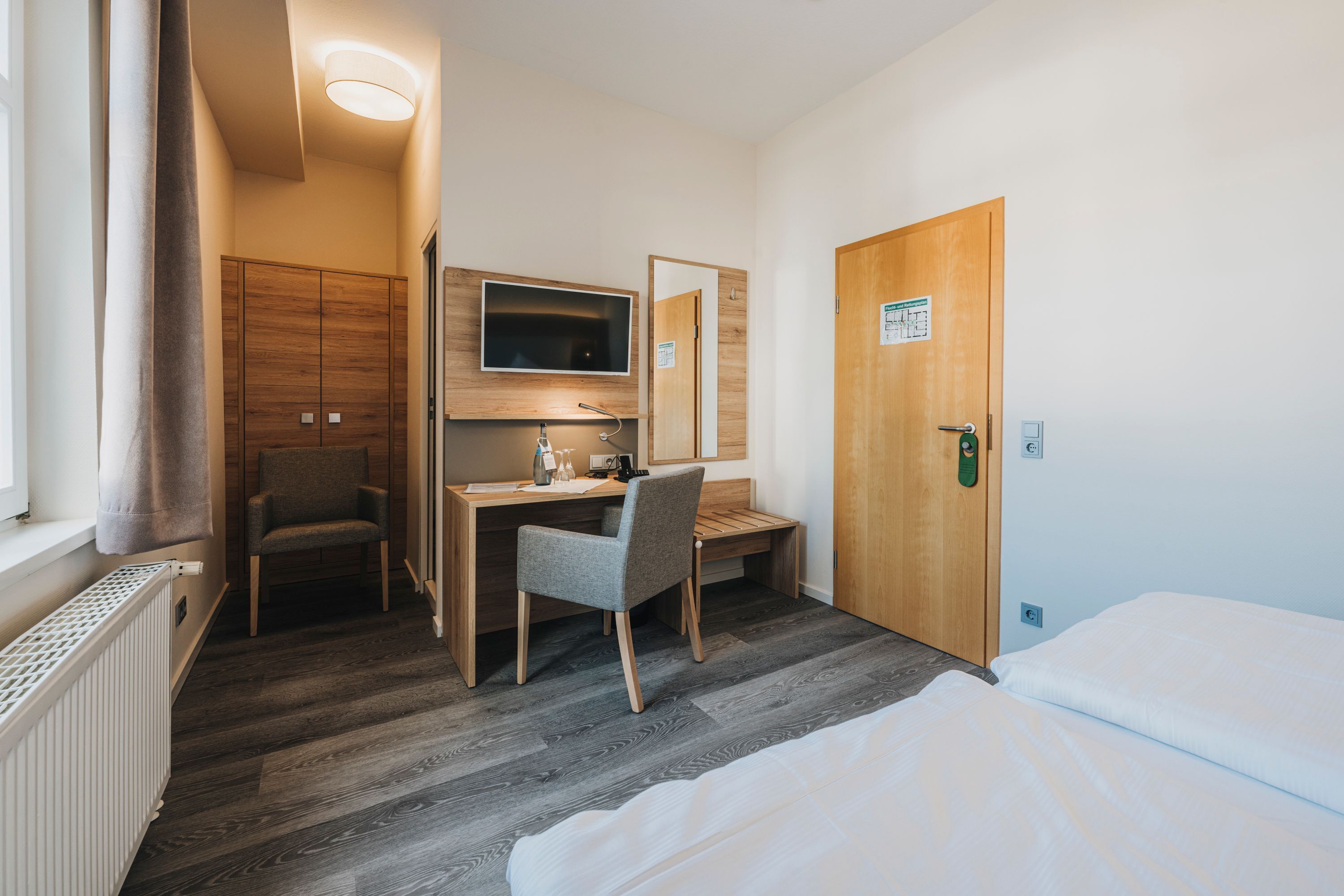 Une chambre d’hôtel comprenant un lit, un bureau avec une chaise, une télévision et une armoire en bois.