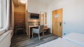 Une chambre d’hôtel comprenant un lit, un bureau avec une chaise, une télévision et une armoire en bois.