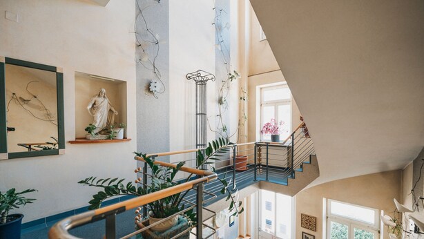 A multi-level interior with a spiral staircase, potted plants, and a statue. - Hotel - Restaurant Roemer (Merzig)