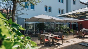 An outdoor patio with tables and chairs, large umbrellas, and potted plants. - Hotel - Restaurant Roemer (Merzig)