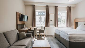 A modern hotel room with a sofa, a desk with a chair, a bed, and a TV mounted on the wall.