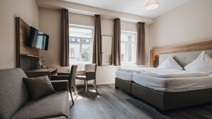 A hotel room with a bed, a sofa, a desk, a TV, and large windows with curtains. - Hotel - Restaurant Roemer (Merzig)