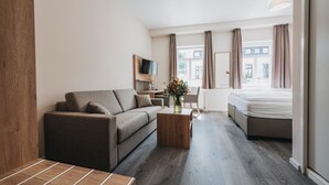 A modern hotel room with a sofa, a small wooden coffee table, a bed, and a TV mounted on the wall. - Hotel - Restaurant Roemer (Merzig)