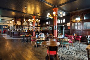 A restaurant with wooden floors, round tables, and red chairs. - The Railway Hotel Worthing (Worthing)