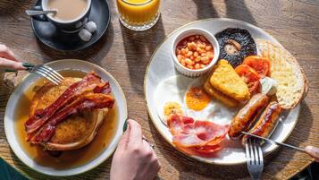 Un desayuno con tortitas, bacon, huevos, salchichas, tostadas y puré de frijoles sobre tostada.