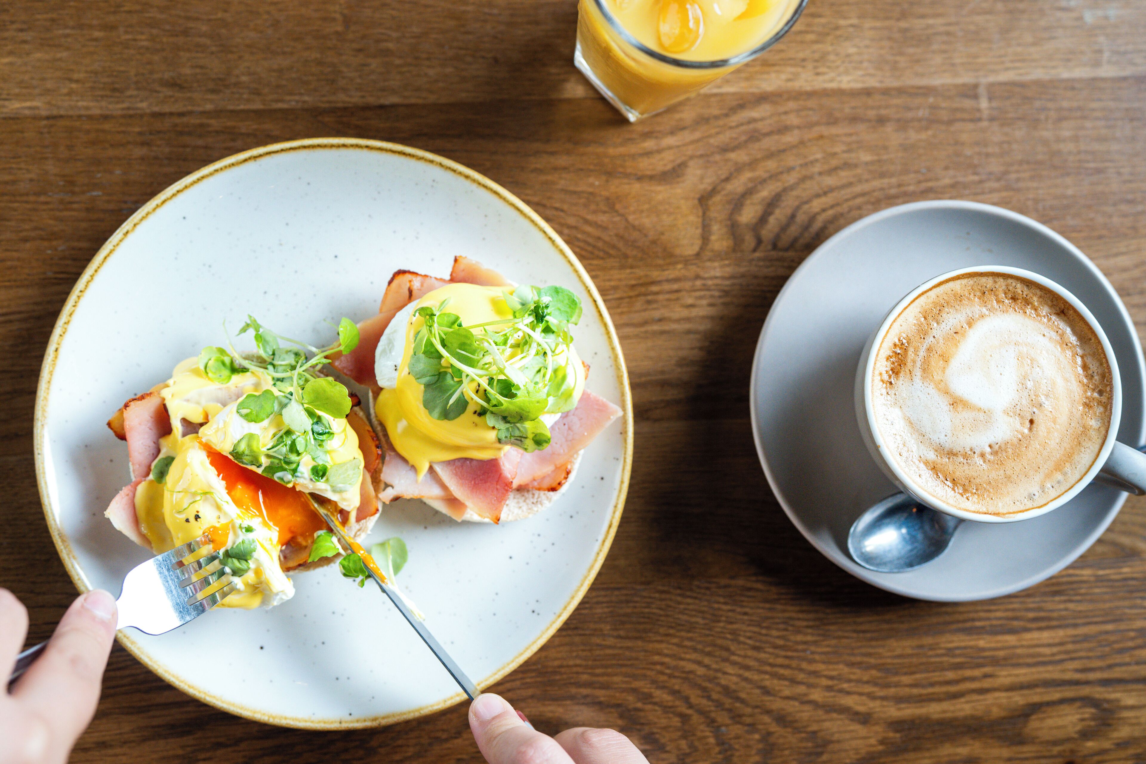 A breakfast setting with a plate of eggs benedict and a cup of coffee on a wooden table.