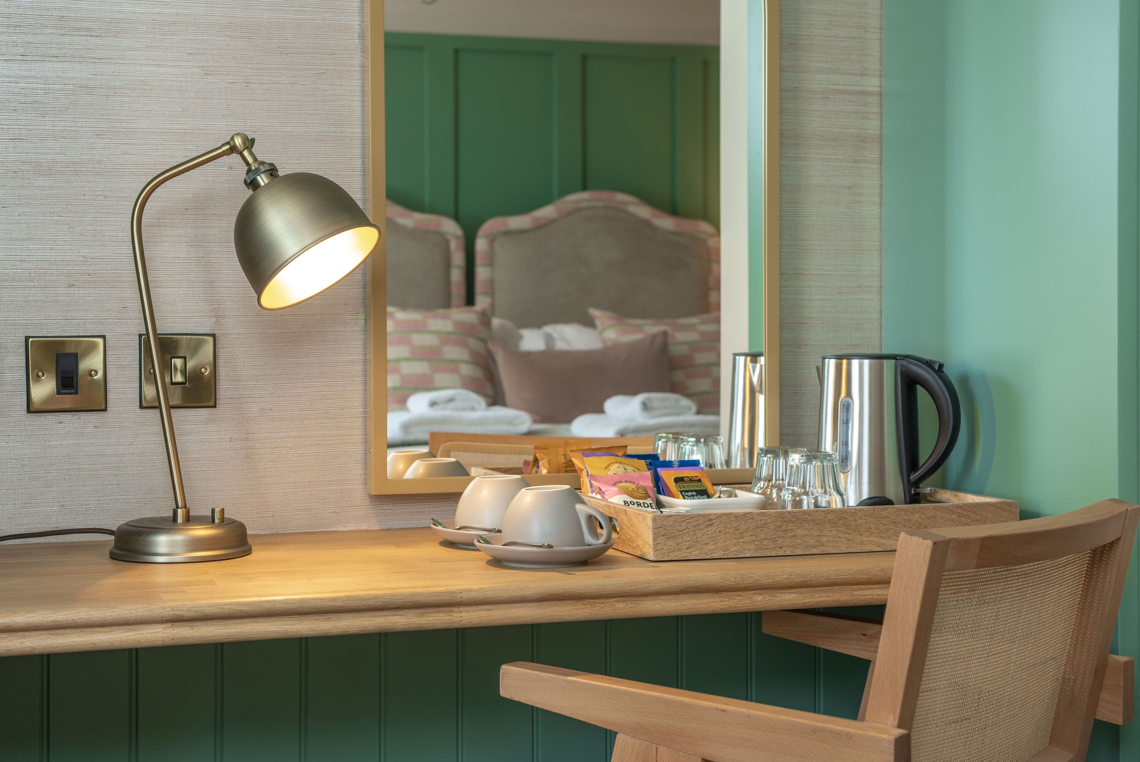 A wooden desk with a lamp, a tray with cups, a box of tissues, and a kettle.