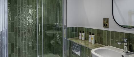 Une salle de bain avec une douche à parois de verre, un lavabo blanc et des murs recouverts de carreaux verts.