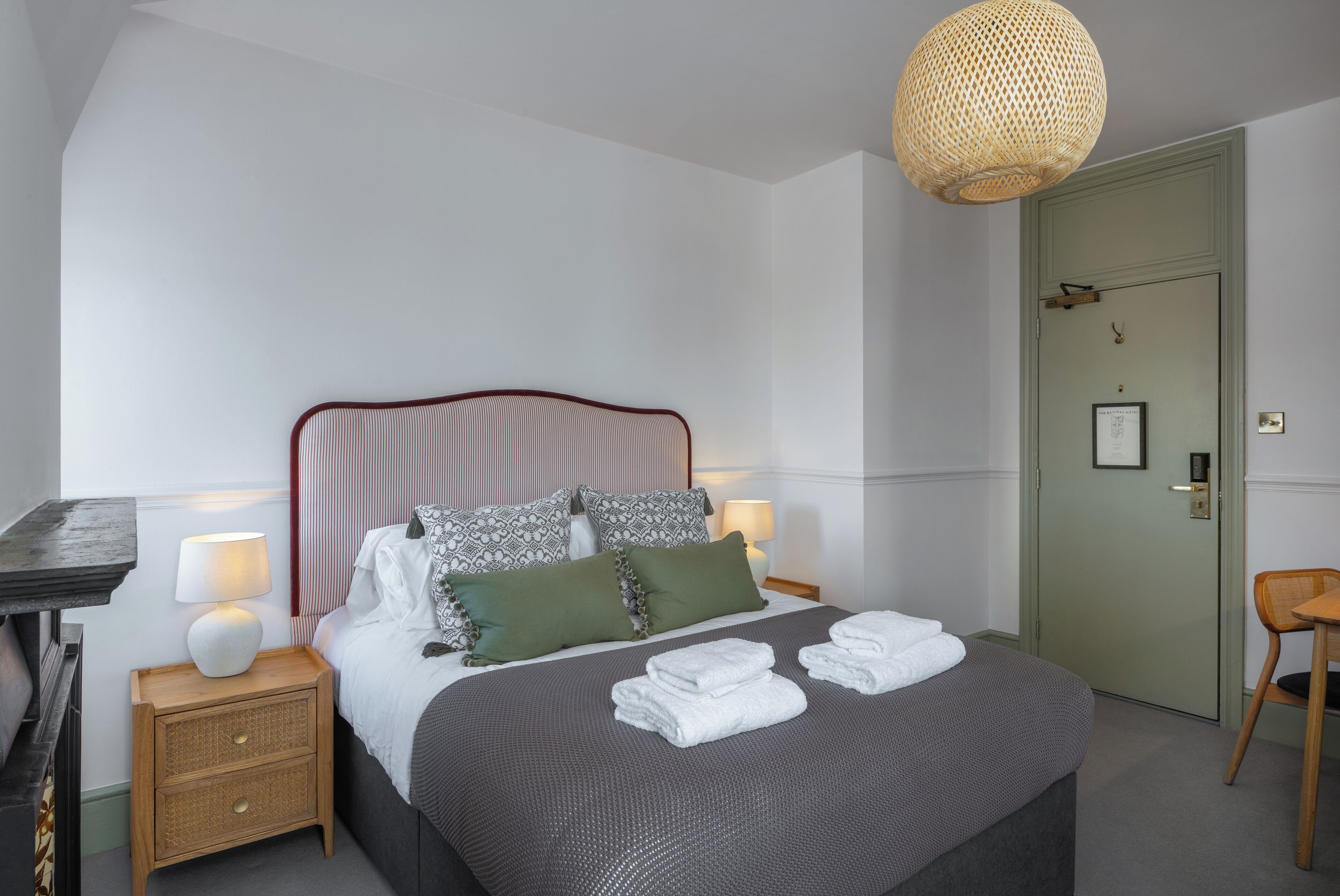 A neatly made bed with pillows, a bedside table with a lamp, and a door with a picture frame.