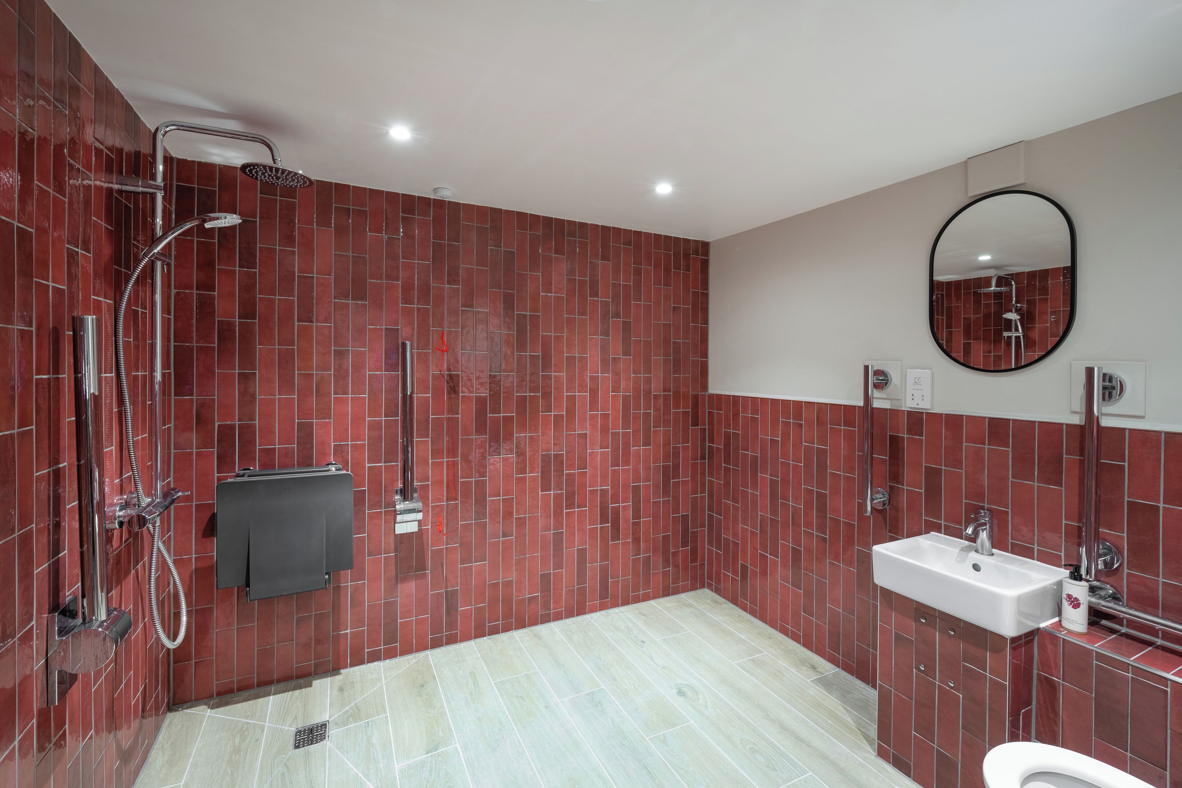 Een moderne badkamer met rode betegelde wanden, een douche, wastafel en toilet.