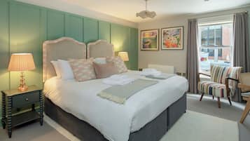 A neatly made bed with pillows and a blanket, a bedside lamp, a chair, and artwork on the wall.