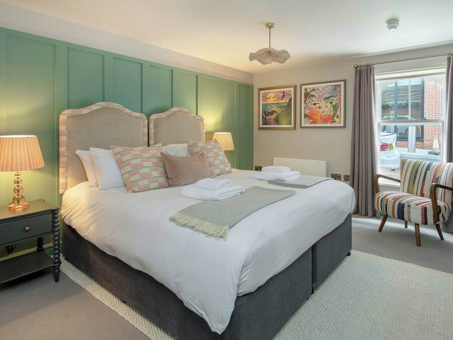 A neatly made bed with pillows and a blanket, a bedside lamp, a chair, and artwork on the wall.