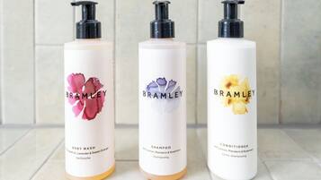 Three bottles of Brambley body wash, shampoo, and conditioner on a tiled surface.