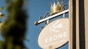 A sign for 'KRONE Restaurant | Hotel' with a crown symbol and a street lamp.