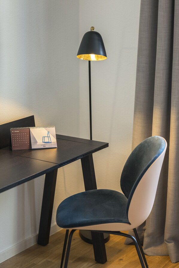 A desk with a calendar, a lamp, and a chair in a room with a wooden floor and curtains.