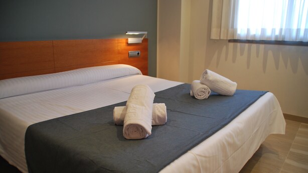 Une chambre d’hôtel avec un grand lit, deux serviettes roulées, une table de chevet avec une lampe et une fenêtre avec des rideaux.