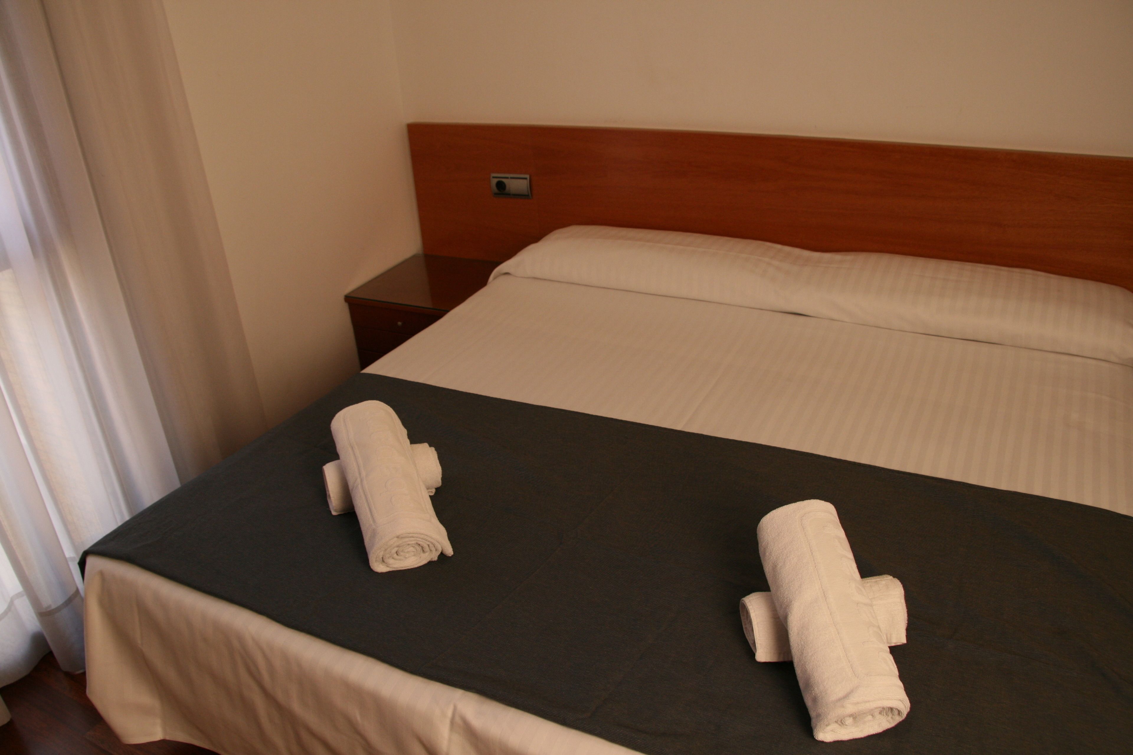 A hotel room with a bed, two towels, a nightstand, and a wooden headboard.