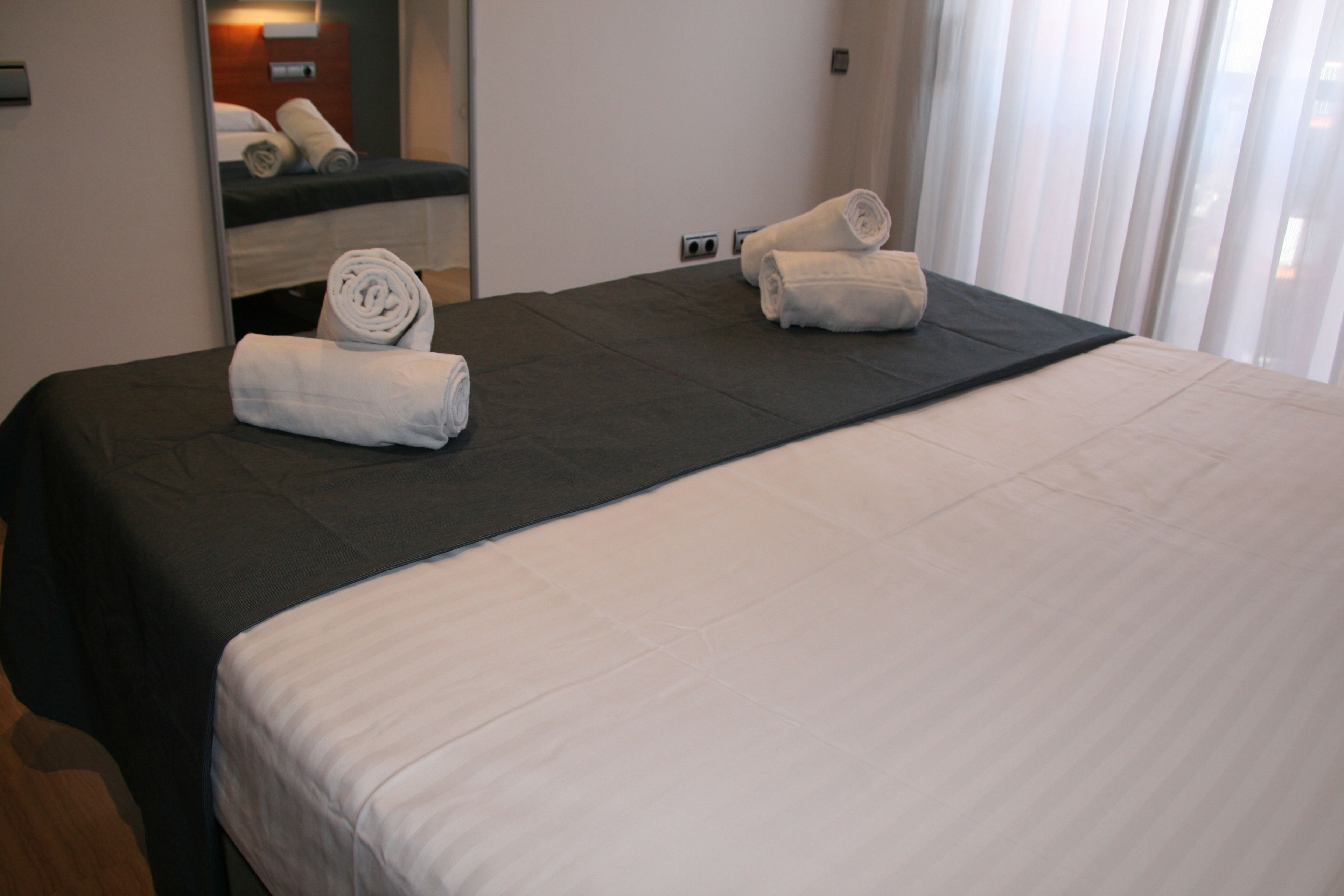 Une chambre d’hôtel avec un grand lit, deux serviettes enroulées, un miroir et une fenêtre avec des rideaux.