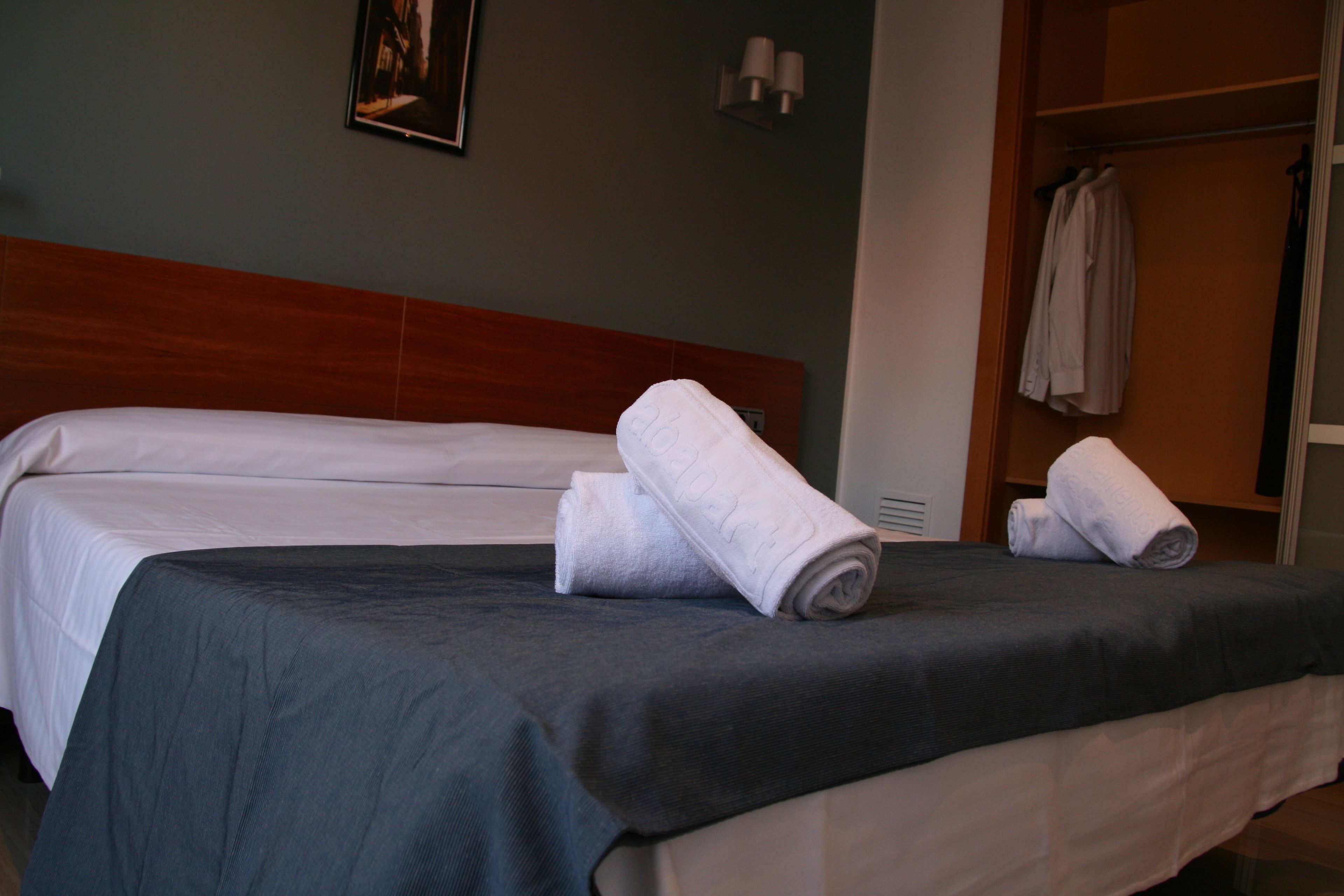 A hotel room with a bed, a wooden headboard, a wall-mounted picture, and a clothing rack with towels.