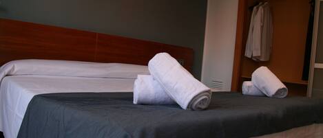 A hotel room with a bed, a wooden headboard, a wall-mounted picture, and a clothing rack with towels.