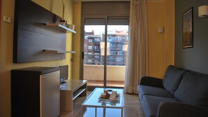 Un salon moderne avec un canapé, une table basse sur laquelle se trouve un plateau avec divers objets, un téléviseur fixé au mur et un balcon offrant une vue sur les bâtiments.