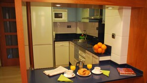 Une petite cuisine équipée d’un évier, d’un four à micro-ondes et d’une machine à café. On y trouve des oranges et un livre sur le plan de travail.