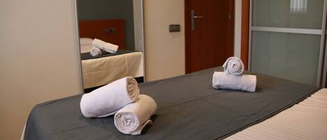 A hotel room with a bed, two rolled towels, a wooden door, and a mirror.