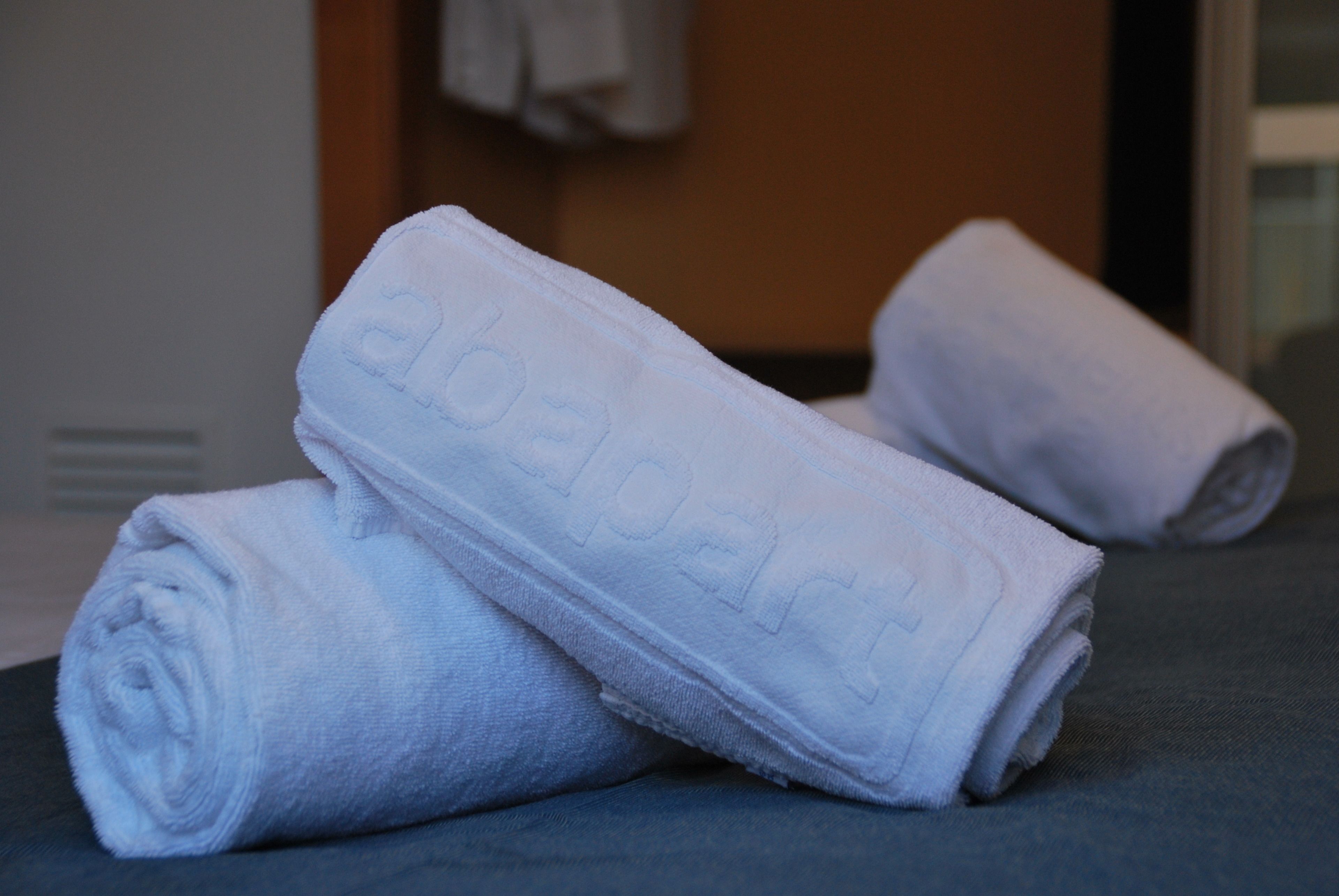 A set of neatly rolled white towels with the word "abapart" embroidered on them, placed on a dark surface.