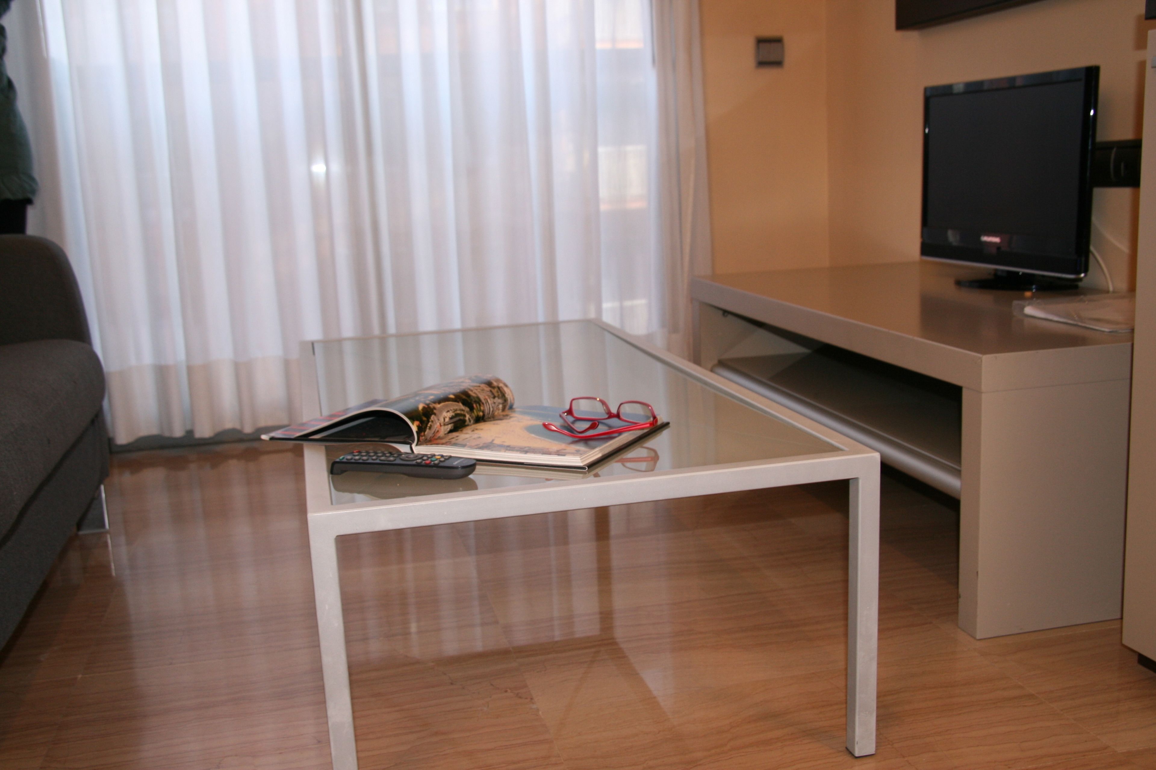 A modern living room with a glass coffee table, a flat-screen TV, and a sofa.
