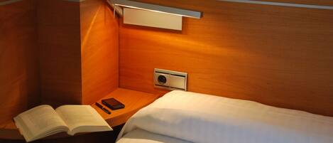 Une chambre d’hôtel avec un lit, une table de chevet sur laquelle repose un livre ouvert, une télécommande et un luminaire fixé au mur.